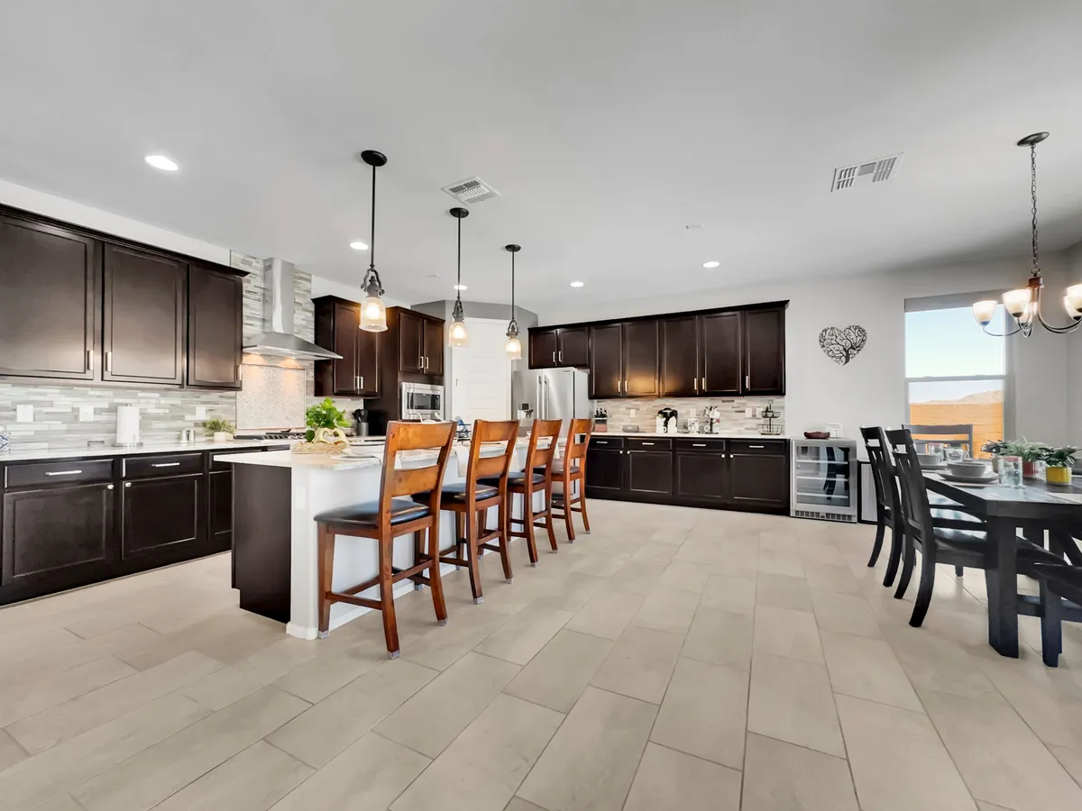 This image features a welcoming kitchen space with a prominent kitchen island surrounded by bar stools. The room is outfitted with modern cabinetry and appliances, and there's a dining table nearby, creating a seamless connection between cooking and dining areas. The open layout allows for plenty of prep space and opportunities for social interaction.