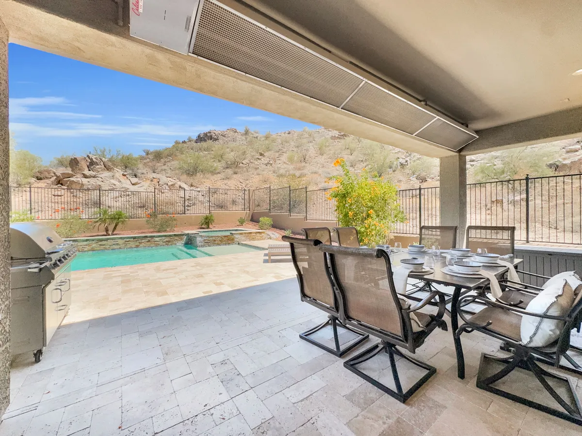A vibrant exterior scene featuring a sparkling swimming pool, an outdoor dining area with a barbecue grill, and sweeping landscape views. Comfortable seating and the inviting grill setup suggest a perfect spot for hosting gatherings and enjoying meals as a group, all against the backdrop of natural beauty.