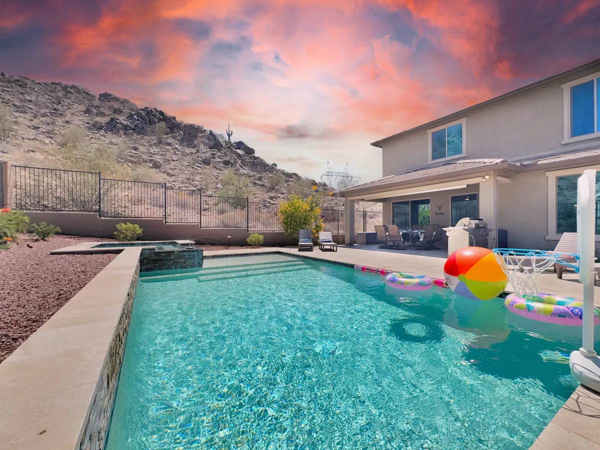A serene backyard scene featuring a sparkling swimming pool surrounded by water floats. The patio area offers comfortable outdoor seating and is framed by lush landscaping, all under the vast Arizona sky. The setting exudes tranquility and an inviting resort-like atmosphere.