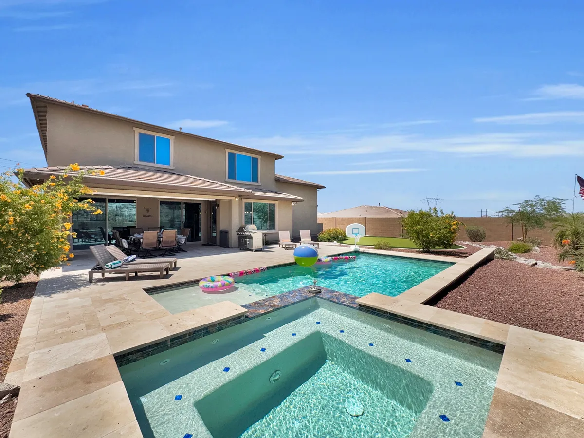 An open, cheerful backyard with a swimming pool, outdoor seating area, and lush landscaping. The arrangement invites families to swim, sunbathe, or simply relax together in a safe, contained environment.