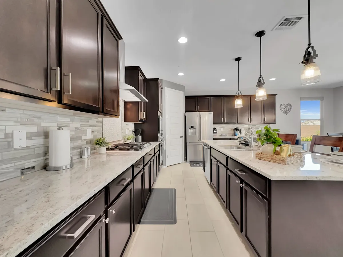 This interior shot focuses on a contemporary kitchen with granite countertops, dark wood cabinetry, modern stainless steel appliances, and stylish pendant lighting. The large kitchen island offers ample prep space and doubles as a spot for informal dining.