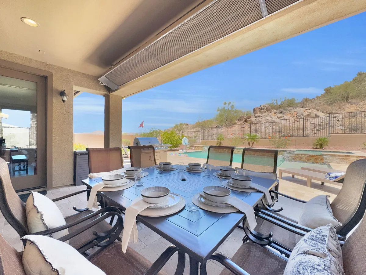 An inviting outdoor dining table set for a meal with a swimming pool and sweeping hills and greenery in the background. The scene evokes a sense of relaxed outdoor living and social gatherings, with a strong connection to nature and the surrounding landscape.