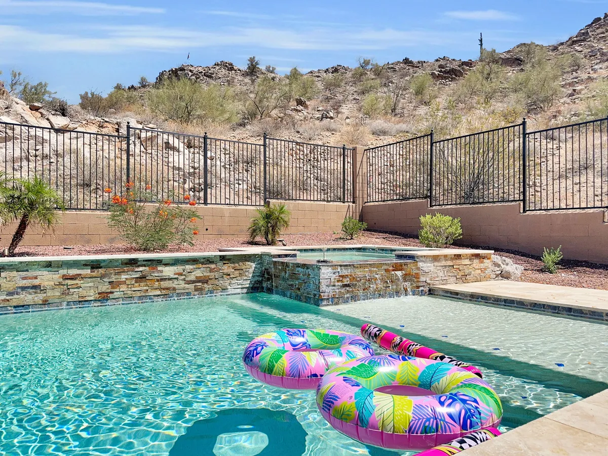 A sunlit pool area with colorful pool floats and a surrounding fence, set against scenic natural landscapes. The scene exudes leisure and playful energy, emphasizing a safe, family-friendly environment for swimming and outdoor play.