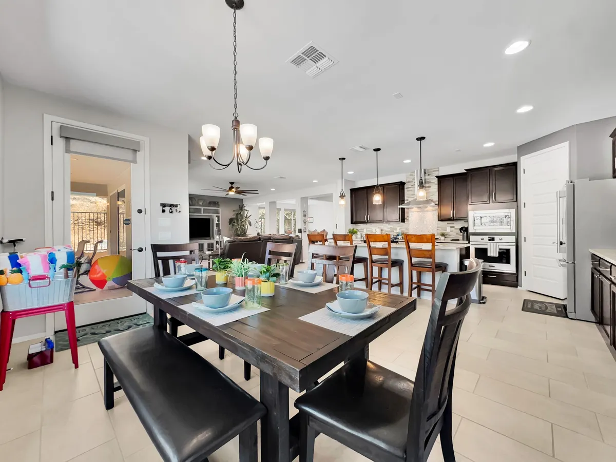 A well-appointed dining table is set for a meal, with the kitchen and modern appliances visible just behind it. The living room is in the background, suggesting an open-concept layout that encourages interaction and connection between spaces.