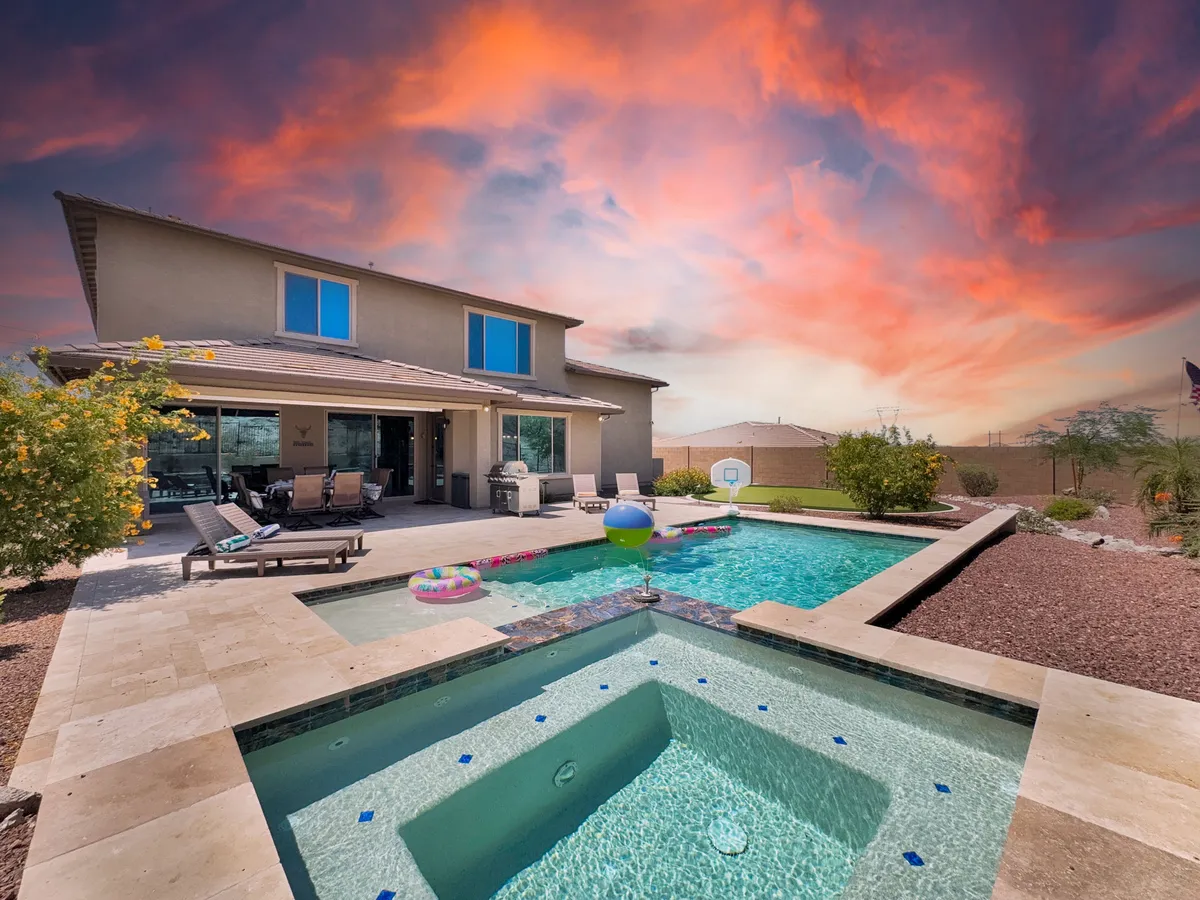 The image features a beautiful swimming pool and spa complemented by patio furniture and lush landscape greenery, all basking under a serene sunset sky. The tranquil setting suggests both joyful gatherings and peaceful evening relaxation by the water.