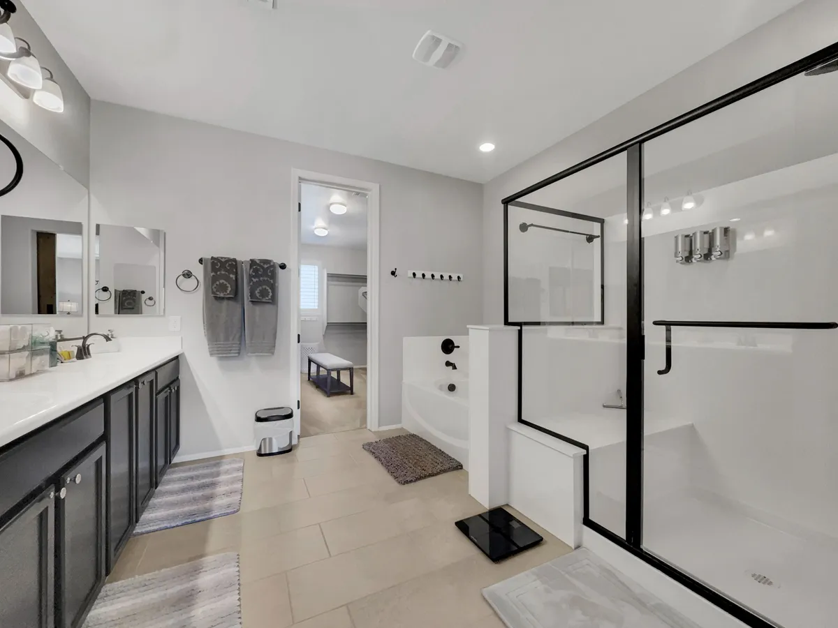 A spacious bathroom featuring a double sink vanity, elegant mirrors, a bathtub, and a glass-enclosed shower. The design is serene and inviting, with plenty of room for self-care routines, and plush towels that reflect the overall luxury of the retreat.