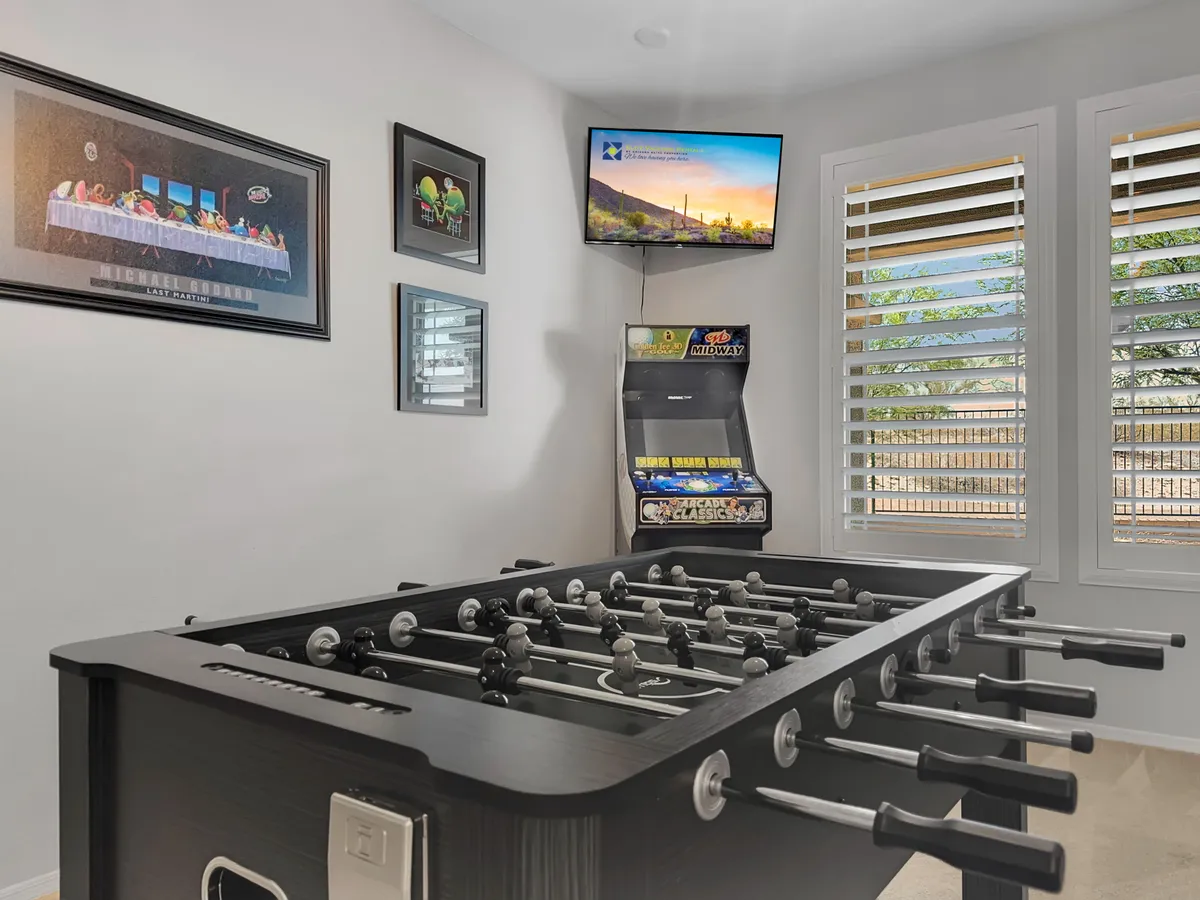 A vibrant game room equipped with a foosball table, an arcade machine, a mounted TV, and colorful wall art. The space is lively and energetic, designed for friendly competition and group fun.
