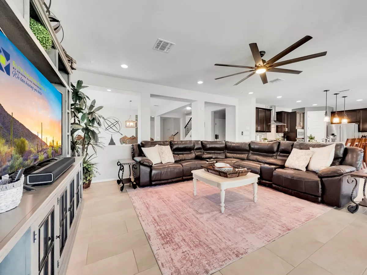 A spacious living area featuring a large sectional sofa, a central coffee table, a television, and decorative plants. The room is styled for comfort and togetherness, ideal for family gatherings, movie nights, or casual group conversations.