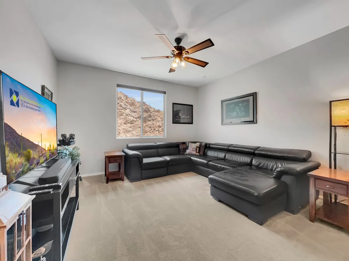A comfortable living space with a leather sectional sofa, a television set in front of a scenic backdrop, and a window framing a view of the mountains. The decor is casual yet inviting, perfect for socializing or enjoying entertainment together.